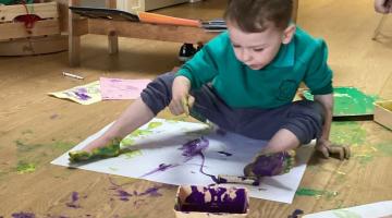 Pre-five boy playing with paint and paper. He has bare feet