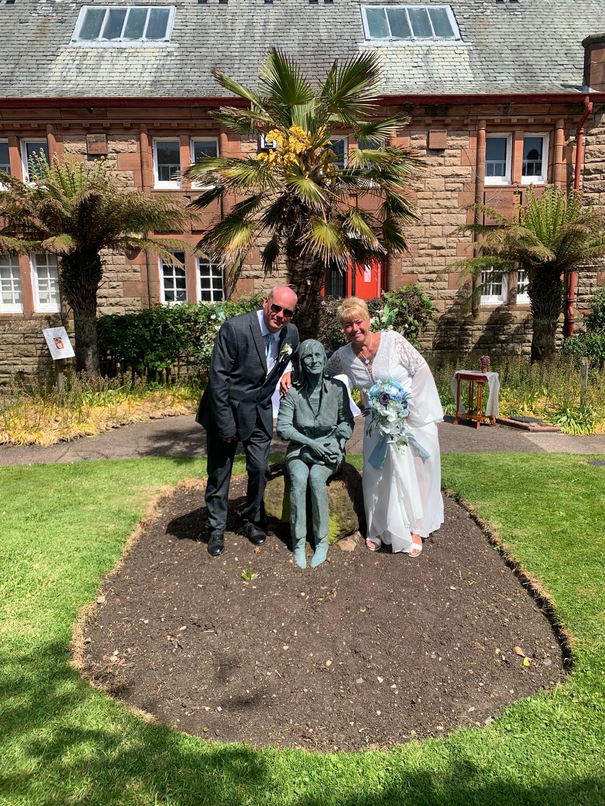 A man and woman in a garden standing next to a statue