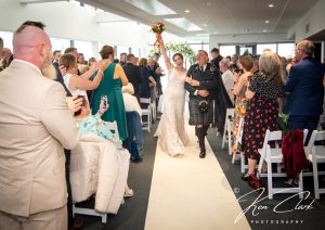 woman holding flowers up in one hand in the air holding mans arm walking up aisle