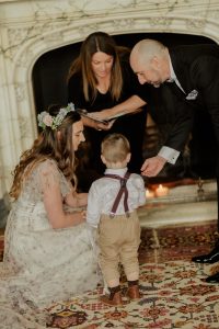 a bride leaning down to a wee boy and a man in a suit helping.
