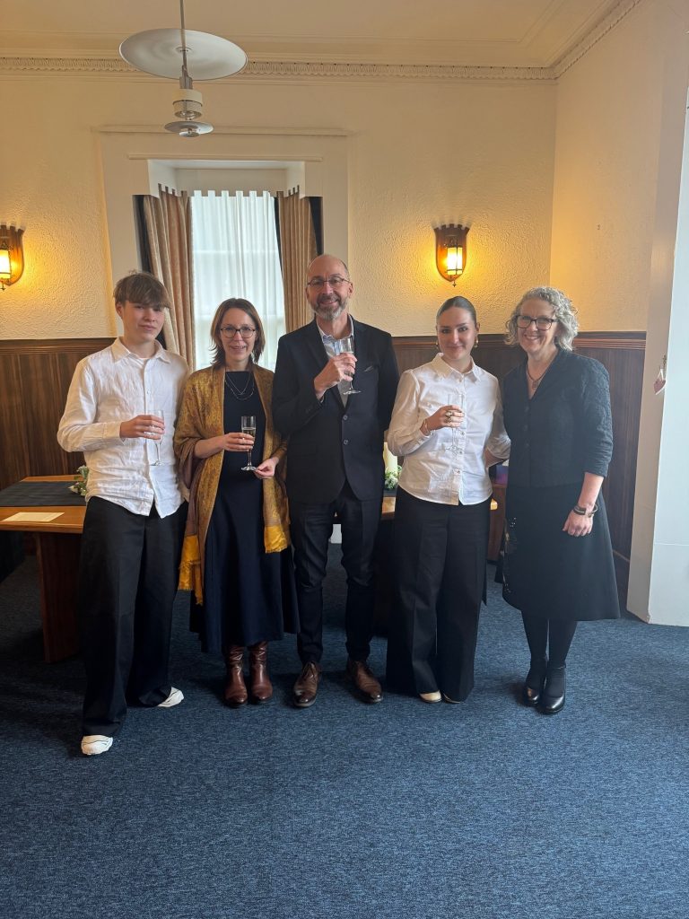 5 people standing in a row in a room 2 male and 3 female