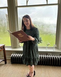 girl in a dress standing in front of a window reading a book