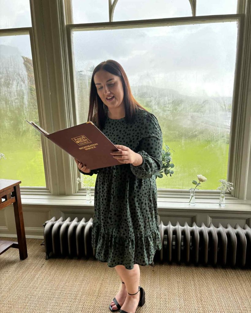 girl in a dress standing in front of a window reading a book