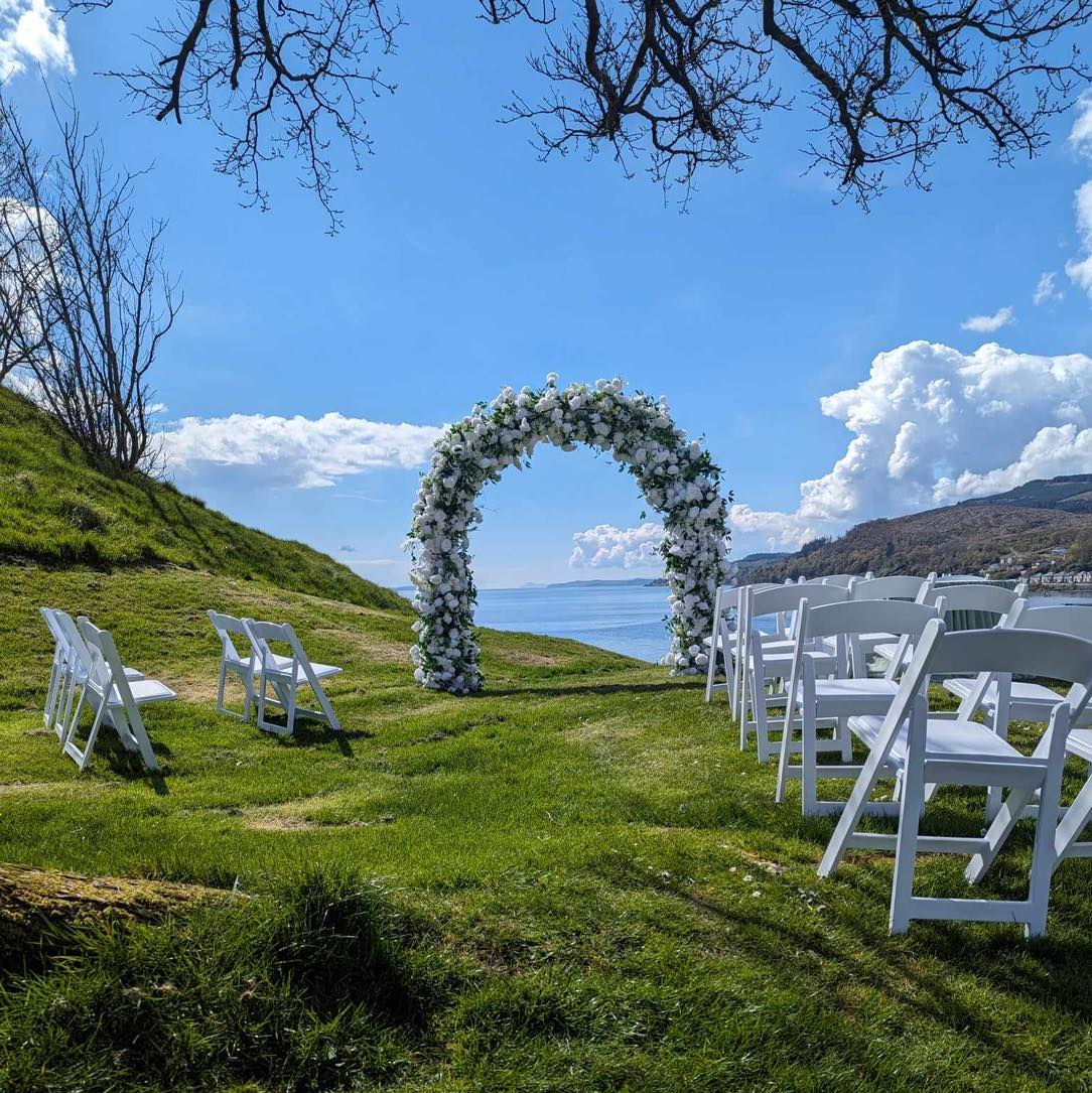 Image showing white wooden chairs set up for a wedding ceremony with an archway with white flowers looking out onto the water