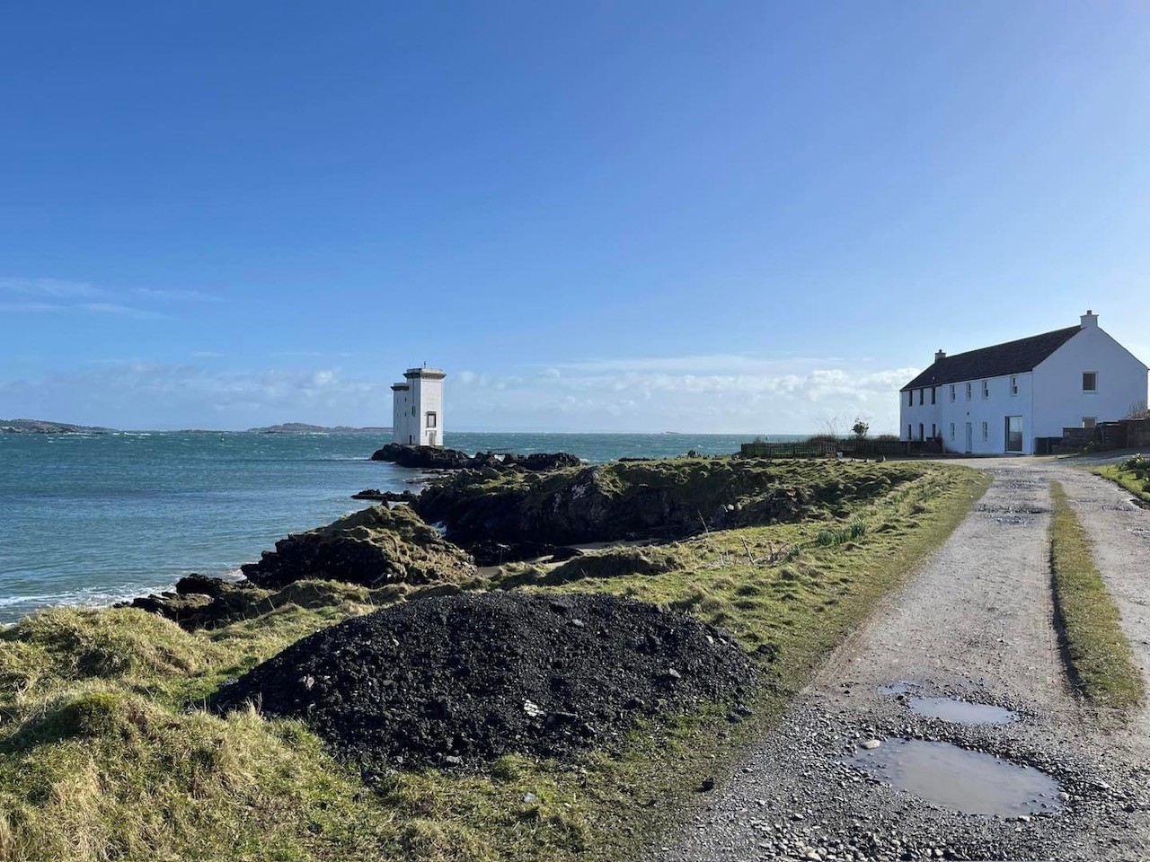 image showing a rocky shoreline with a white house and a lighthouse in the background