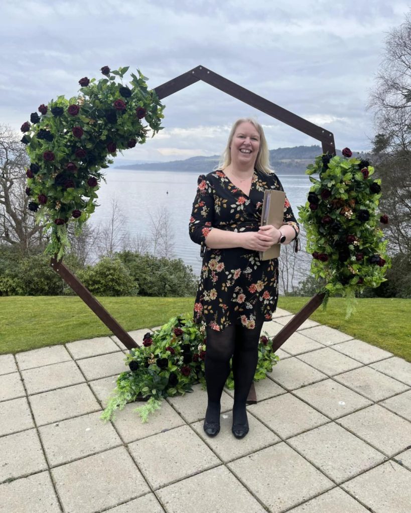 Woman in dress standing holding book in front of arch