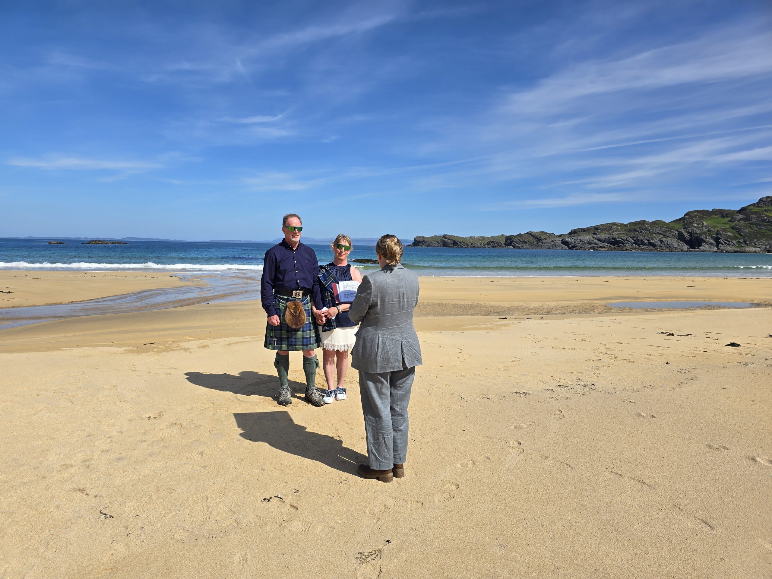 2 woman and 1 man standing on a beach blue sky
