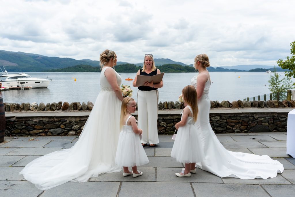 2 woman in bridal dresses in front of a woman by the water