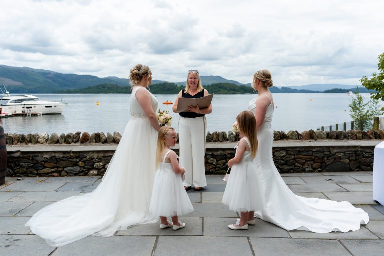 2 woman in bridal dresses in front of a woman by the water