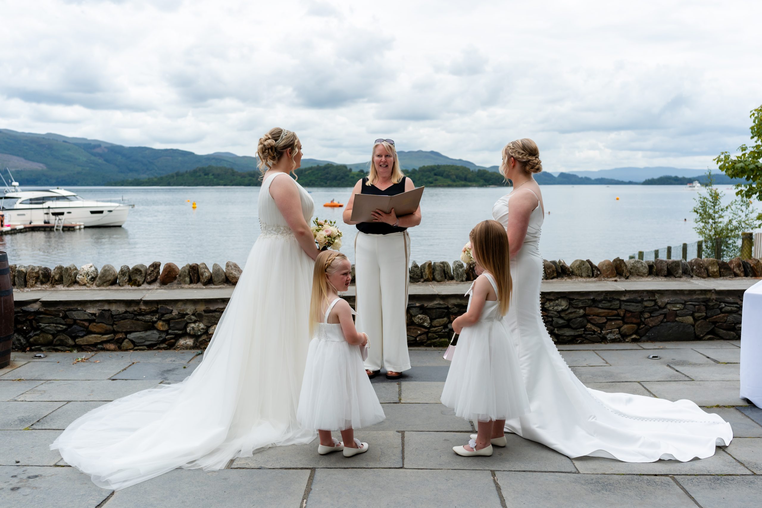 2 woman in bridal dresses in front of a woman by the water