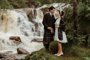 man and a woman standing on rocks with a waterfall in the background