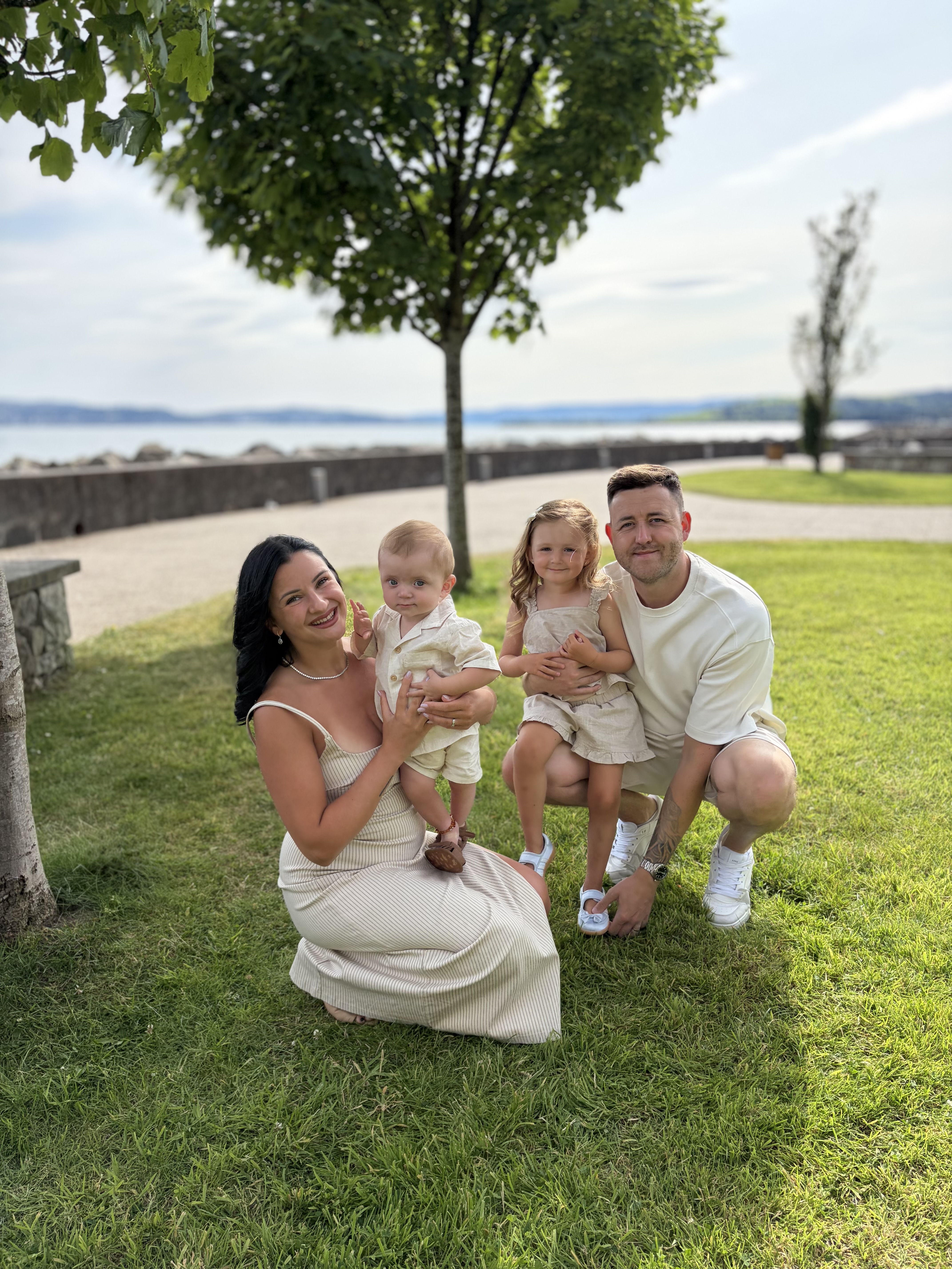 man woman and 2 children bent down with tree behind them