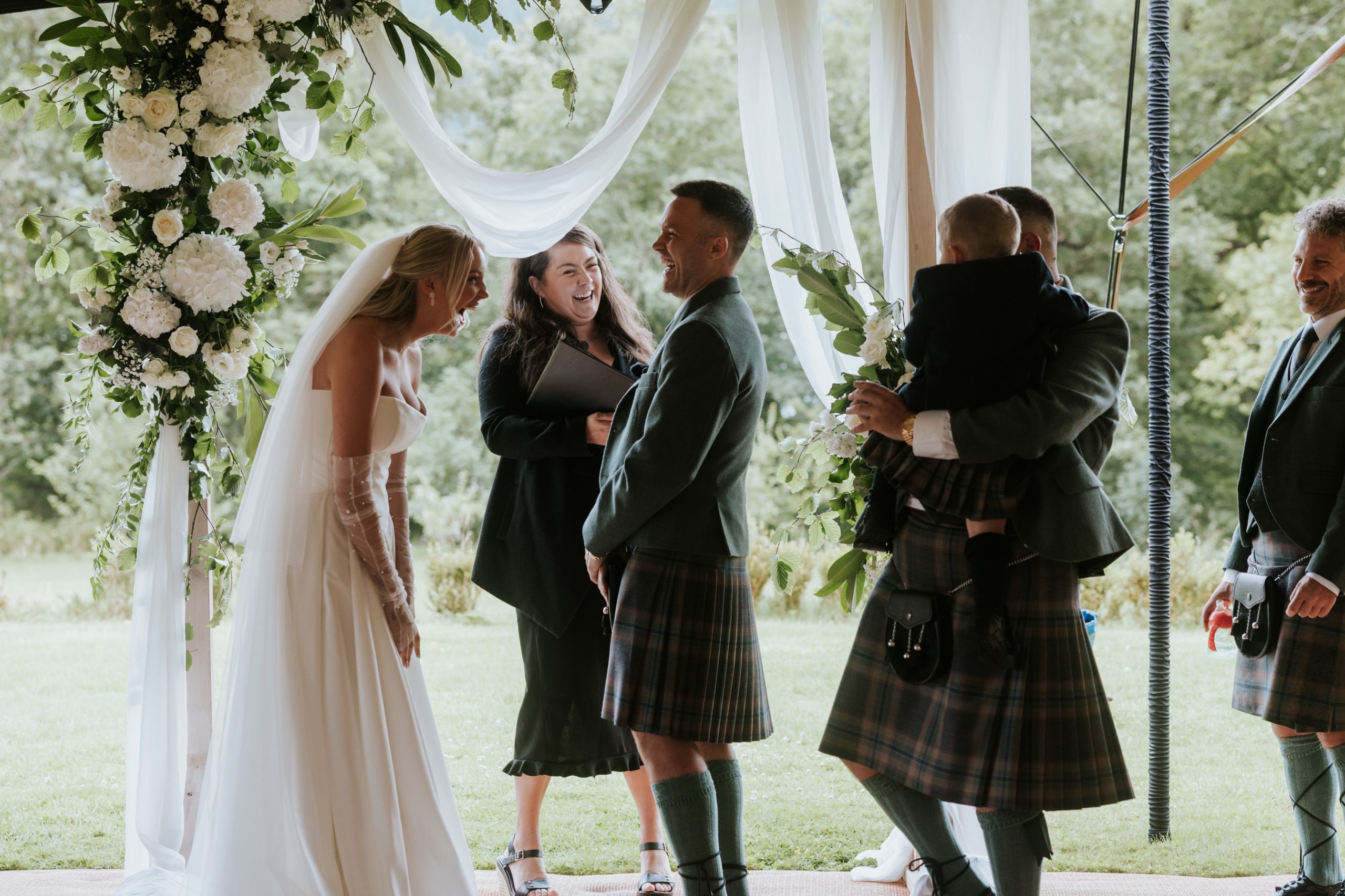 2 men in kilts under flower arch with 2 woman all laughing