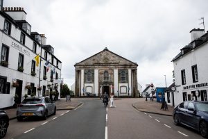 a street with a big building at the top and a man and woman walking down the middle