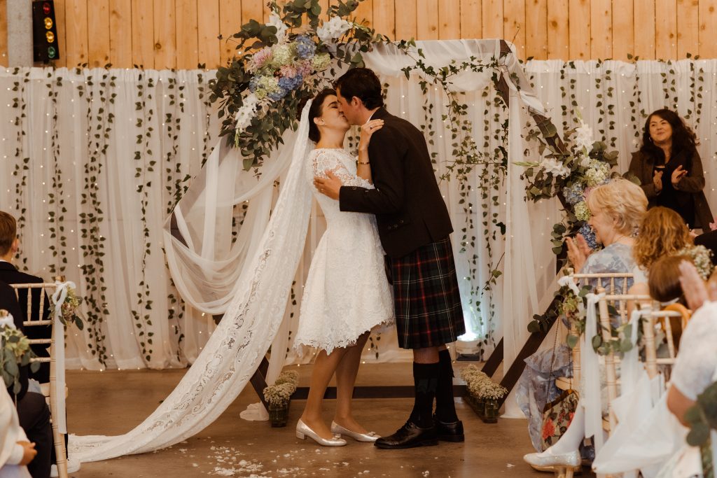 man and woman kissing in front of flower circle arch
