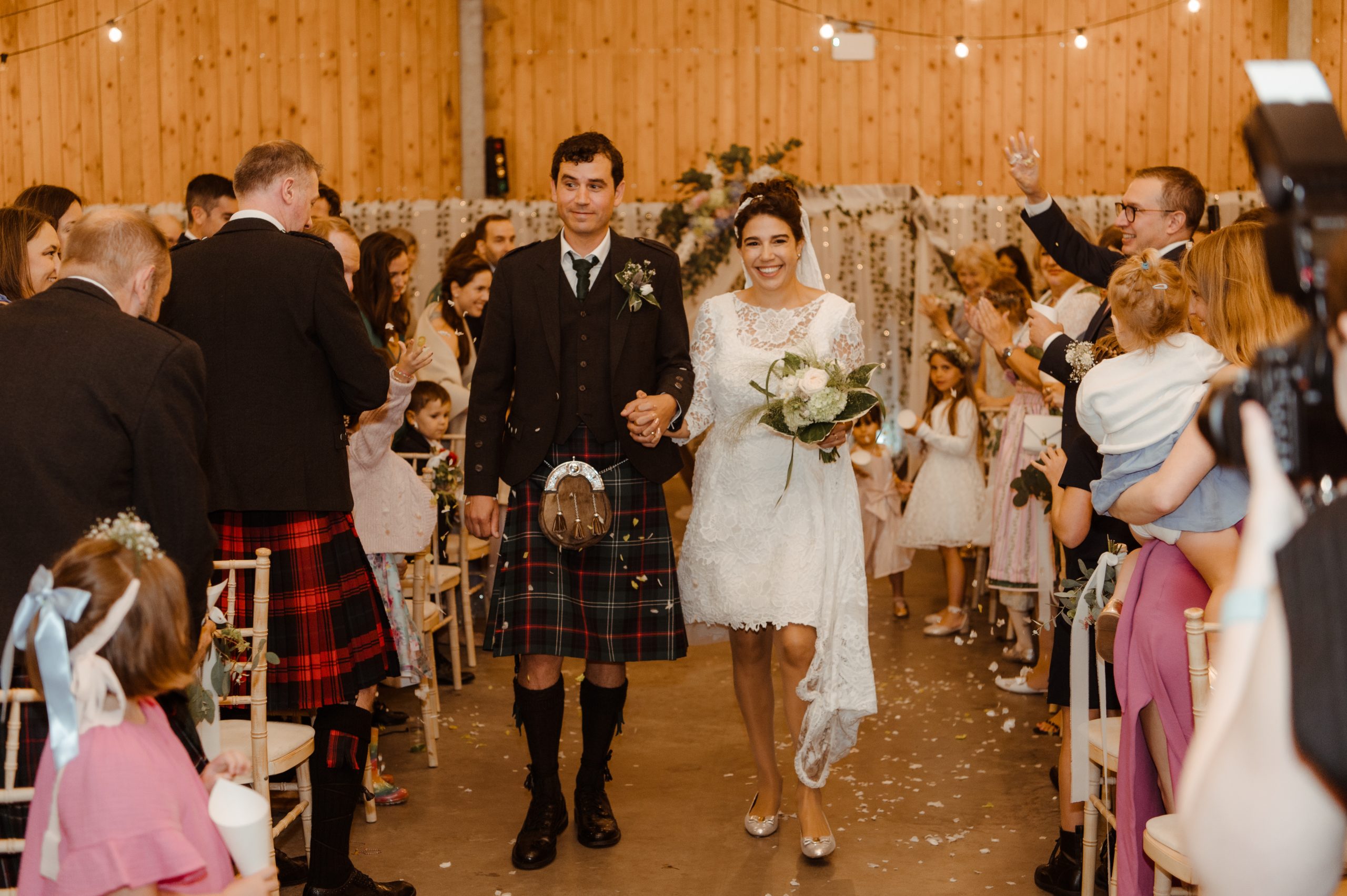 barn with an aisle man in kilt and woman in white short dress walking up the middle