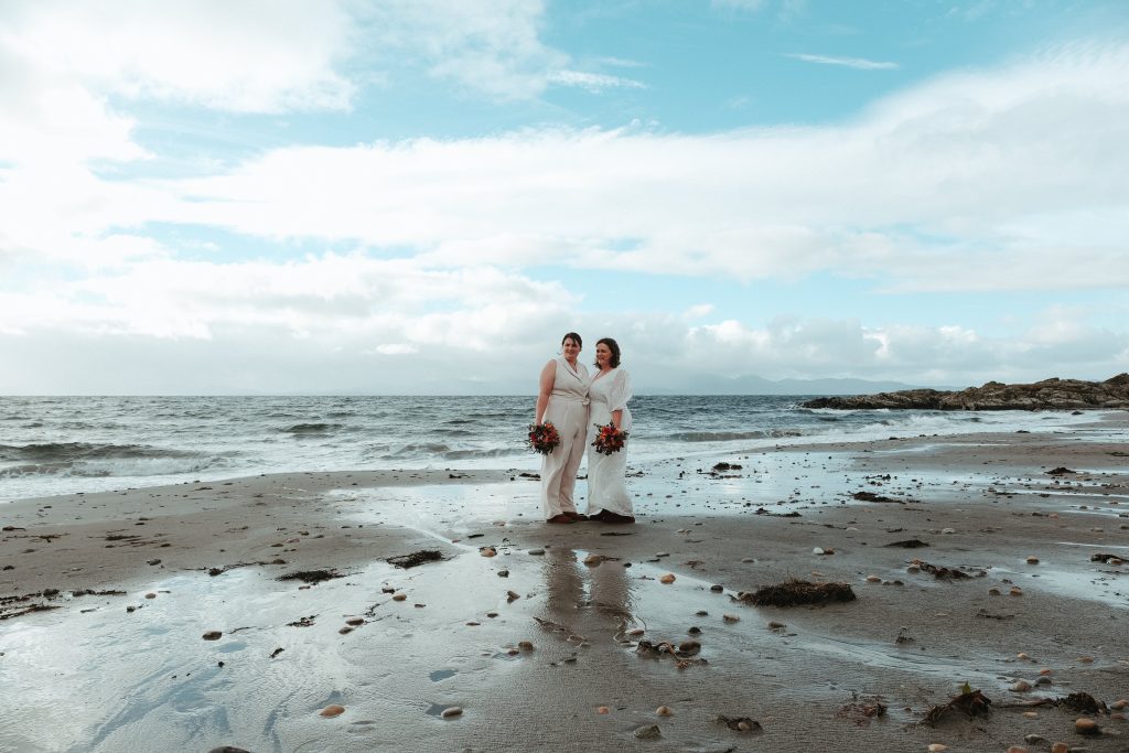 2 woman standing in white outfits on the beach