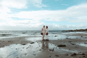 2 woman standing in white outfits on the beach