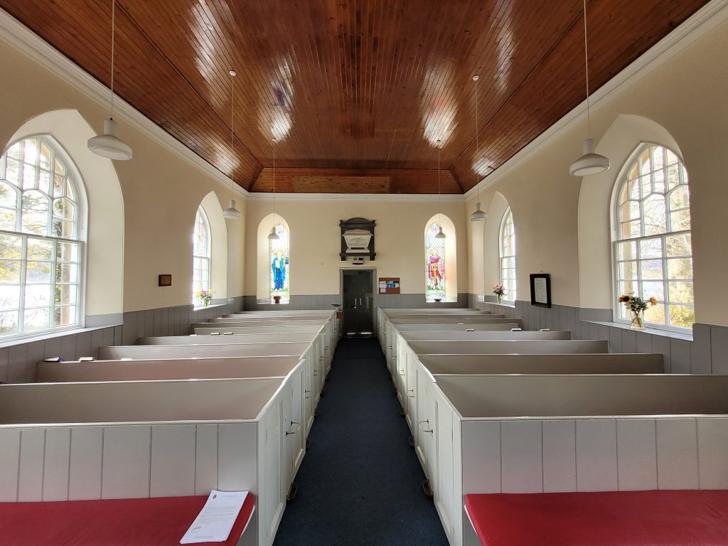 Image of the inside of a church style building with rows of wooden benches