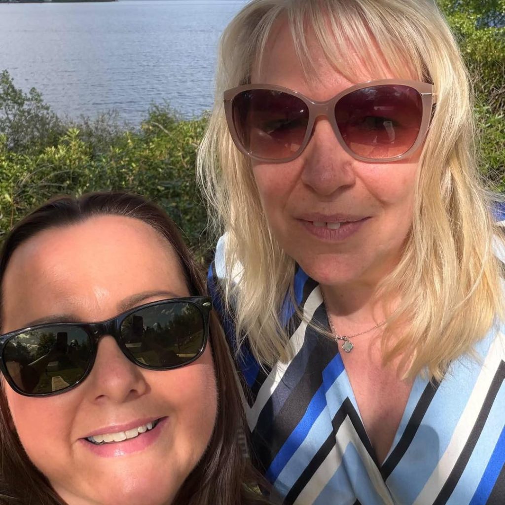 2 woman taking a selfie one with blonde hair the other with dark hair both wearing sunglassess