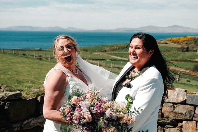 A white in a white dress holding bouquet of flowers next to a woman in a white suit