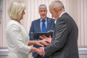 Blonde woman in a white suit holding hands with a man in a dark suit. Man in blue suit in the middle