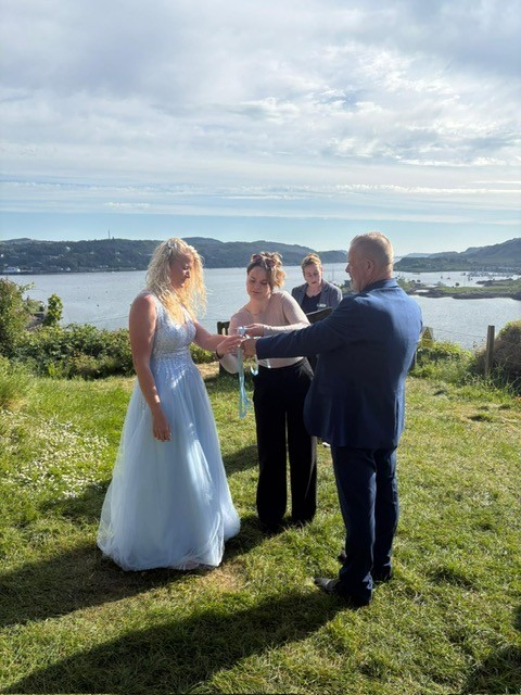 3 Woman and a man standing on a grass area with water in the background