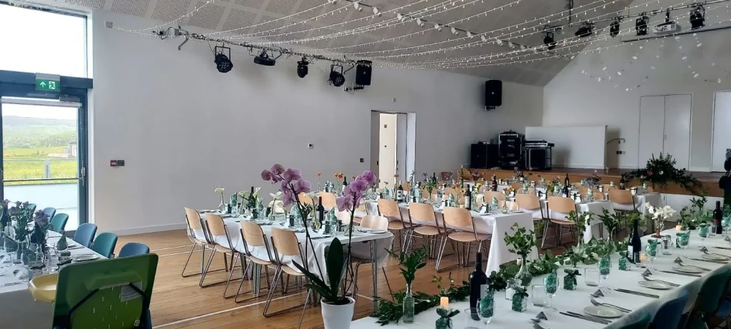 Image of a large room set up with tables and chairs for a wedding reception with floral decorations