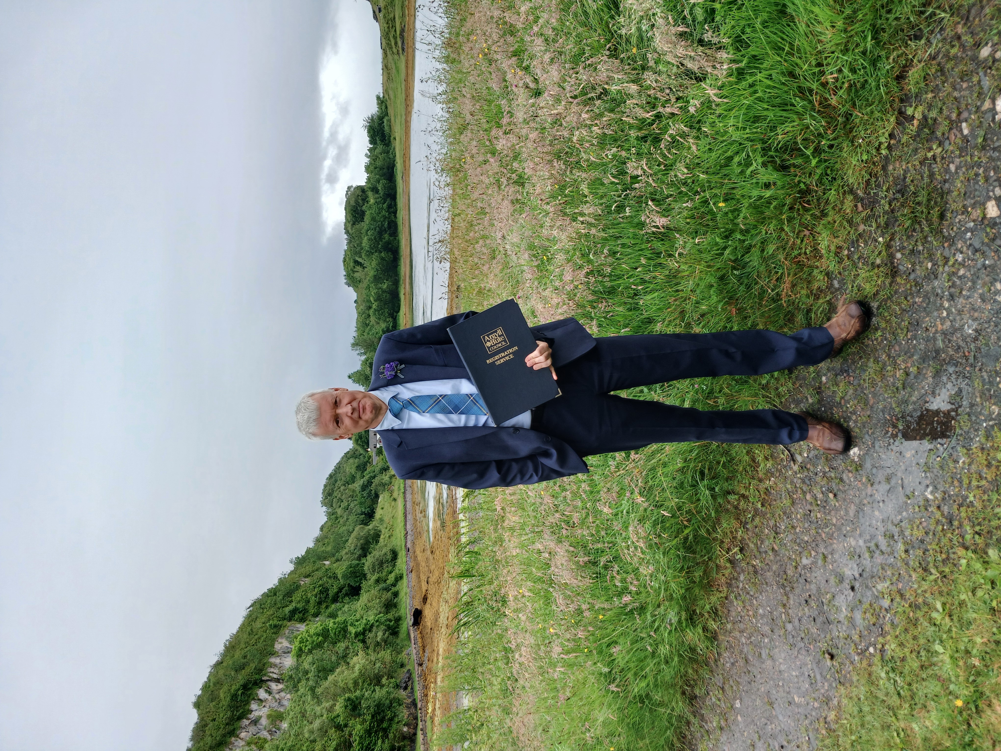 A man in a suit standing next to grass and by water