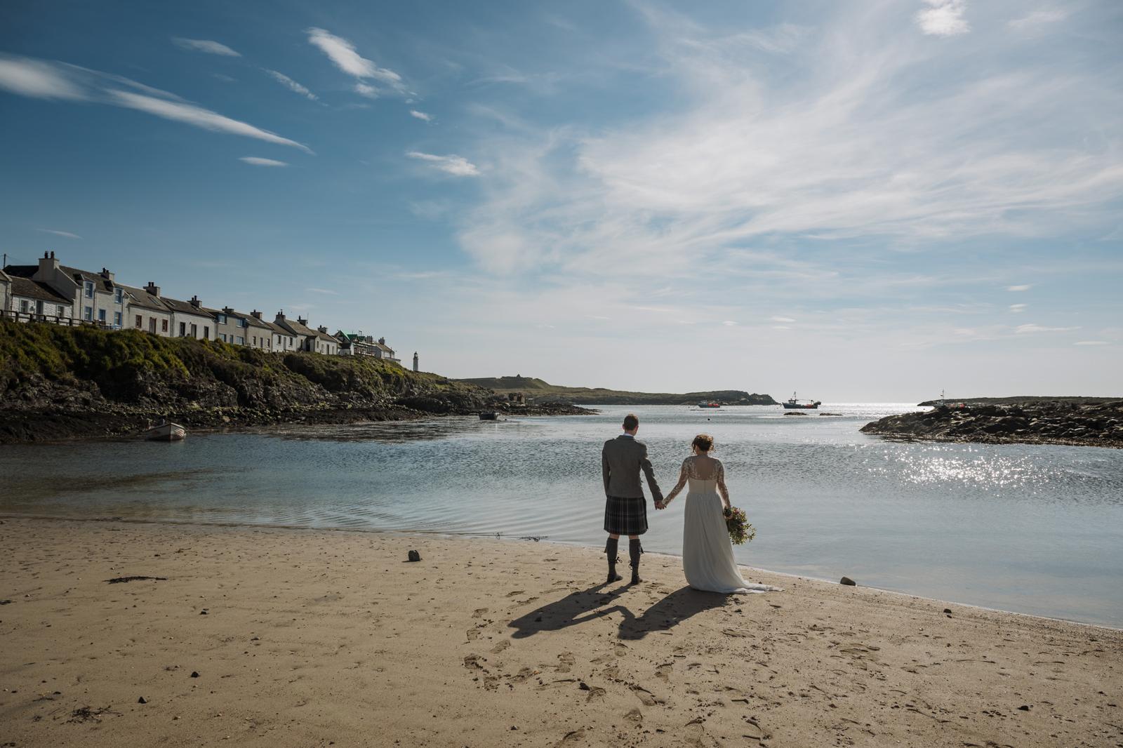 A bride and groom on a beach facing away