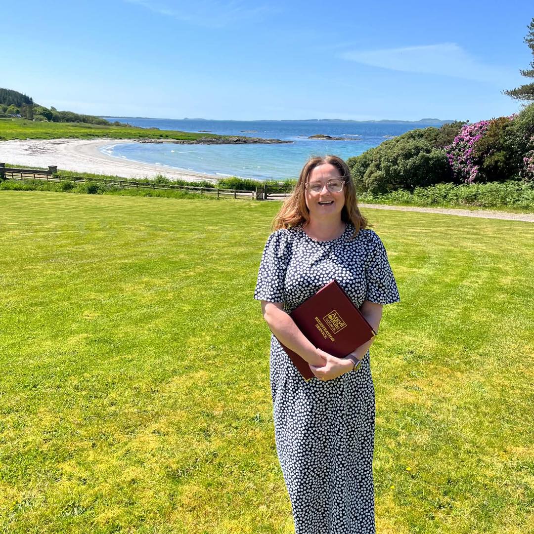 Woman in a blue dress standing on grass with beach behind her