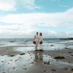 2 woman standing in white outfits on the beach
