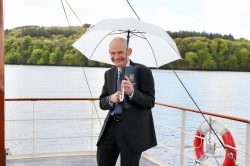 a man in a dark suit on a boat standing under a white umbrella