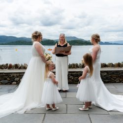 2 woman in bridal dresses in front of a woman by the water