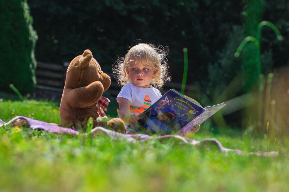Toddler reading with teddy bear on picnic blanket