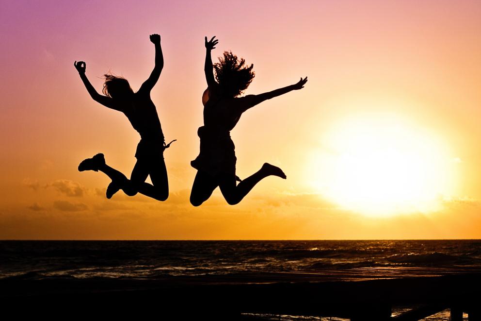 Images shows the silhouette of two young people jumping in the air against a sunset background 