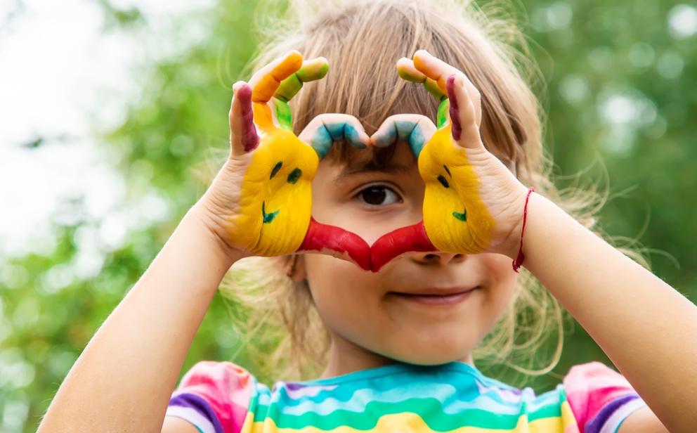 Image shows a young girl holding her painted hands in a heart shape