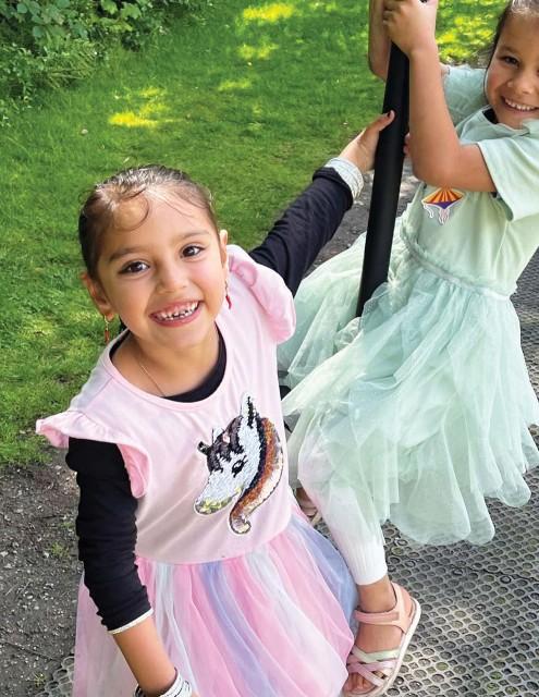 Image shows two girls, one on a rope swing smiling 
