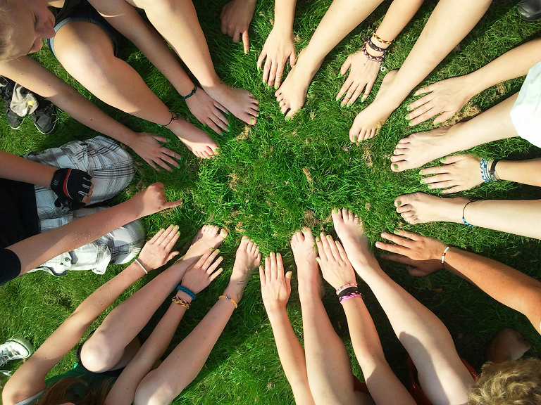 a group of people sitting on grass with their hands in a circle