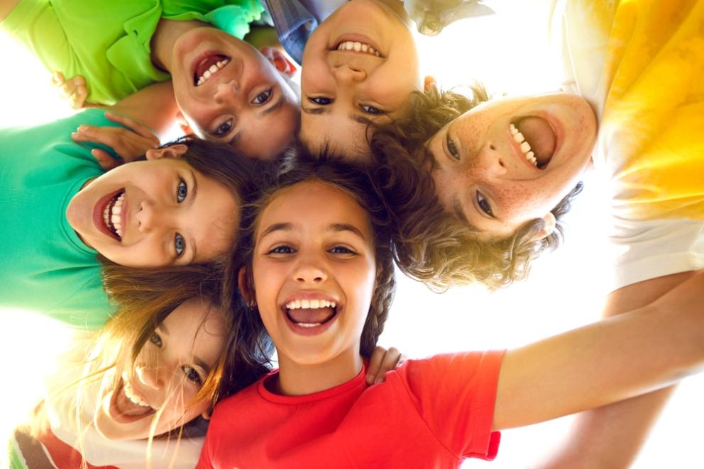 Group portrait of happy kids huddling, looking down at camera and smiling.