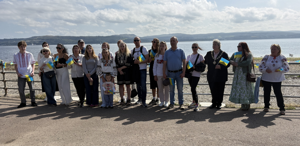 A group of people stand in front of the railings at the sea front in Dunoon