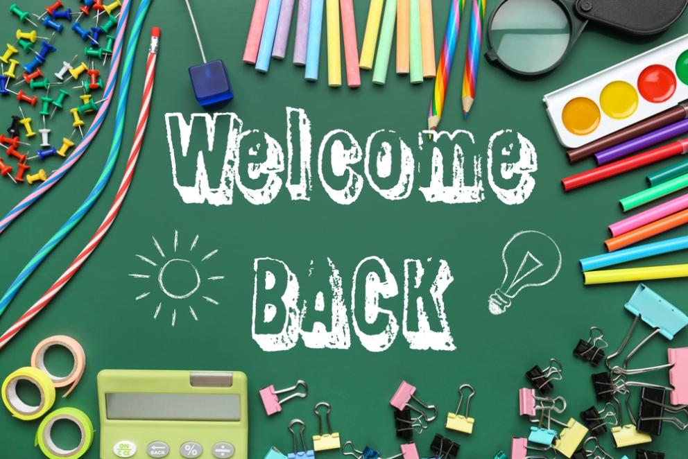 Image shows a green welcome back sign with different bits of stationery around the sides including pencils and paint