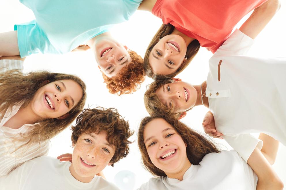 Image shows a group of six teenagers in a circle smiling looking down the camera 
