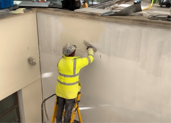 Worker applying render top coat to east and south facing wall surrounds.