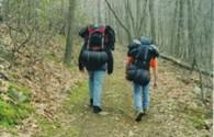 2 walkers with large bags walking along woodland trail