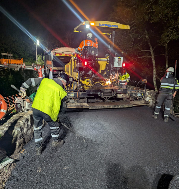 Workmen lay the final surface on the bridge, with machinery in the background
