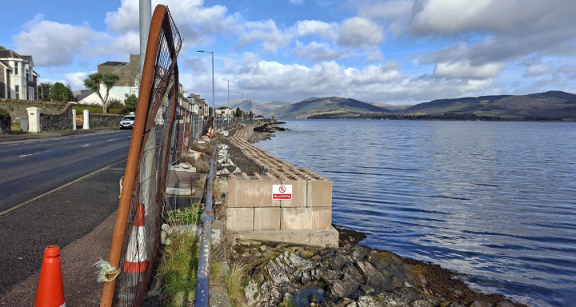 Ardbeg wall before works started. View of blockwork along shore with heras fencing along the edge of the footway