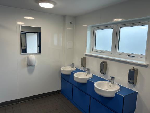 3 sinks along blue unit with hand dryer and mirror on side wall