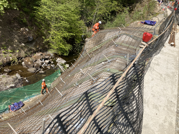 Workers on the side of an embankment. They are laying the reinforcement bars in preparation of the shotcrete.  Soil nails have been fully installed, as can be seen by the steel bars sticking out the face of the slope.