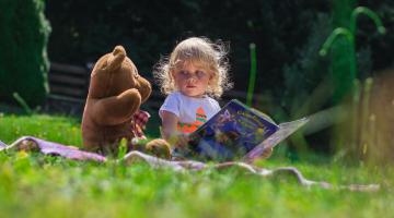 Toddler reading with teddy bear on picnic blanket